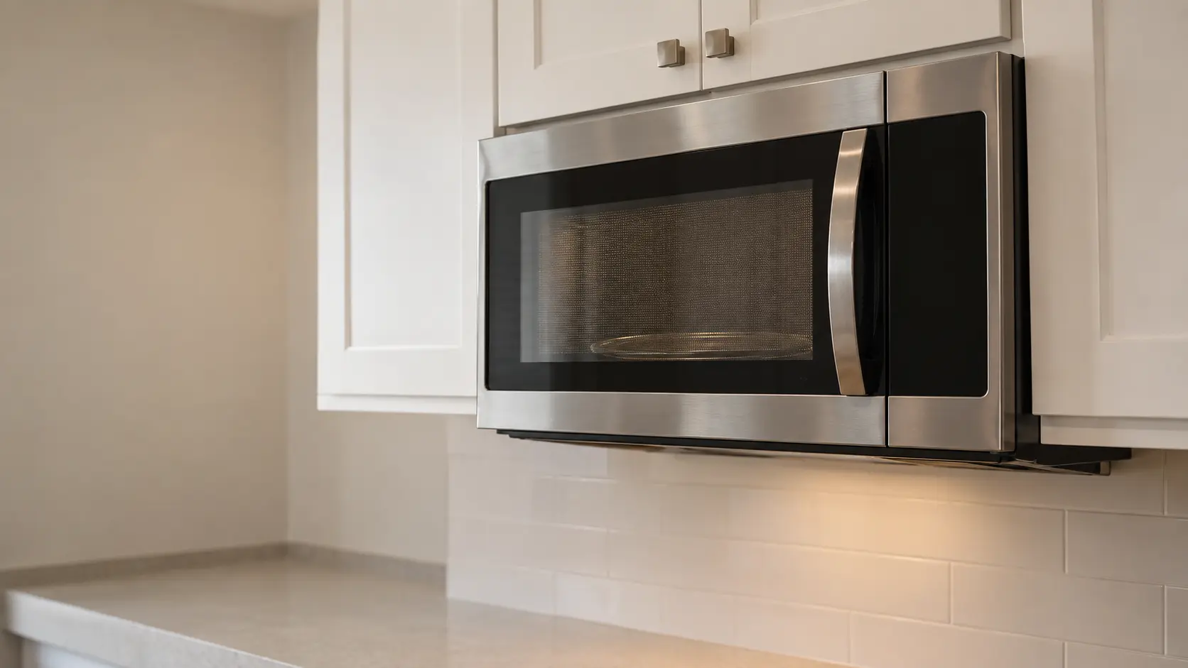 A kitchen with a microwave hood combination under wall cabinets and white shaker cabinets, seen close and low at the microwave's door.
