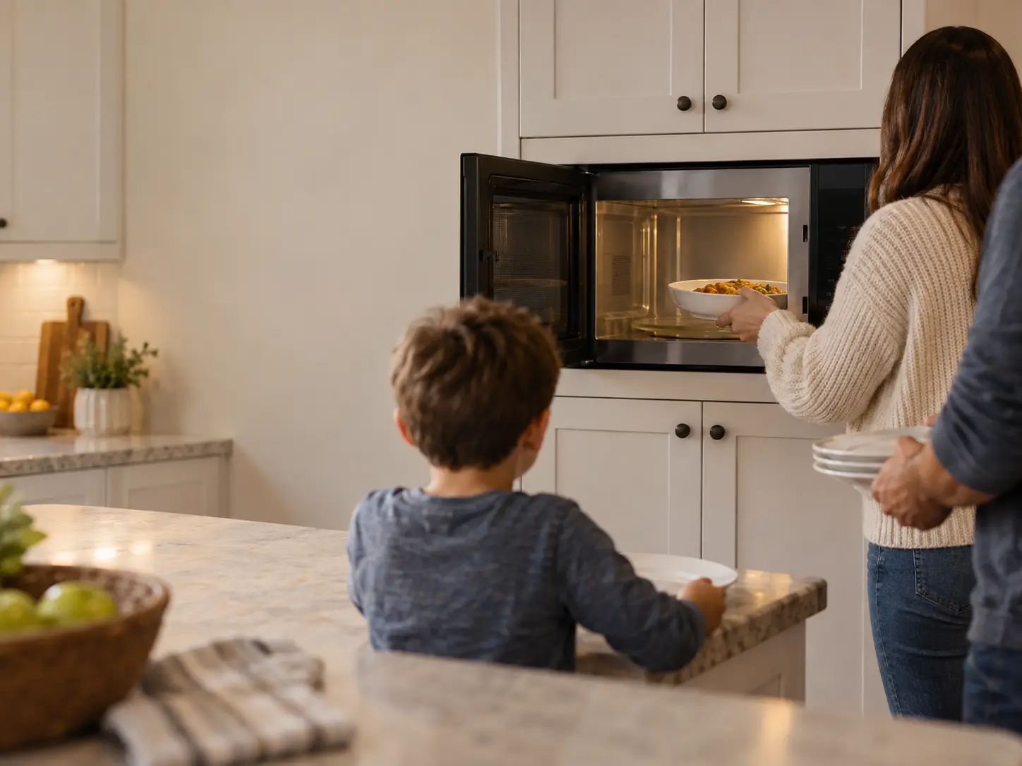 A family warming plates of food at a built-in microwave in a bright kitchen