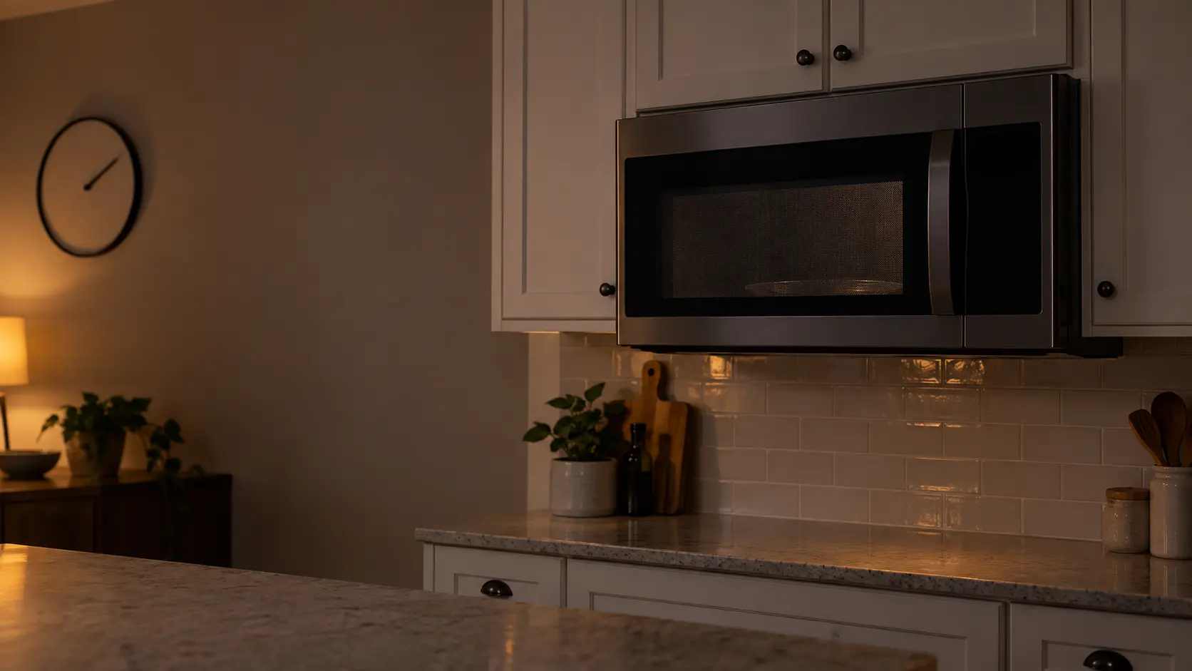 A microwave hood combination under wall cabinets with a dark display just after a power cut, a kitchen clock on the wall behind showing the evening.